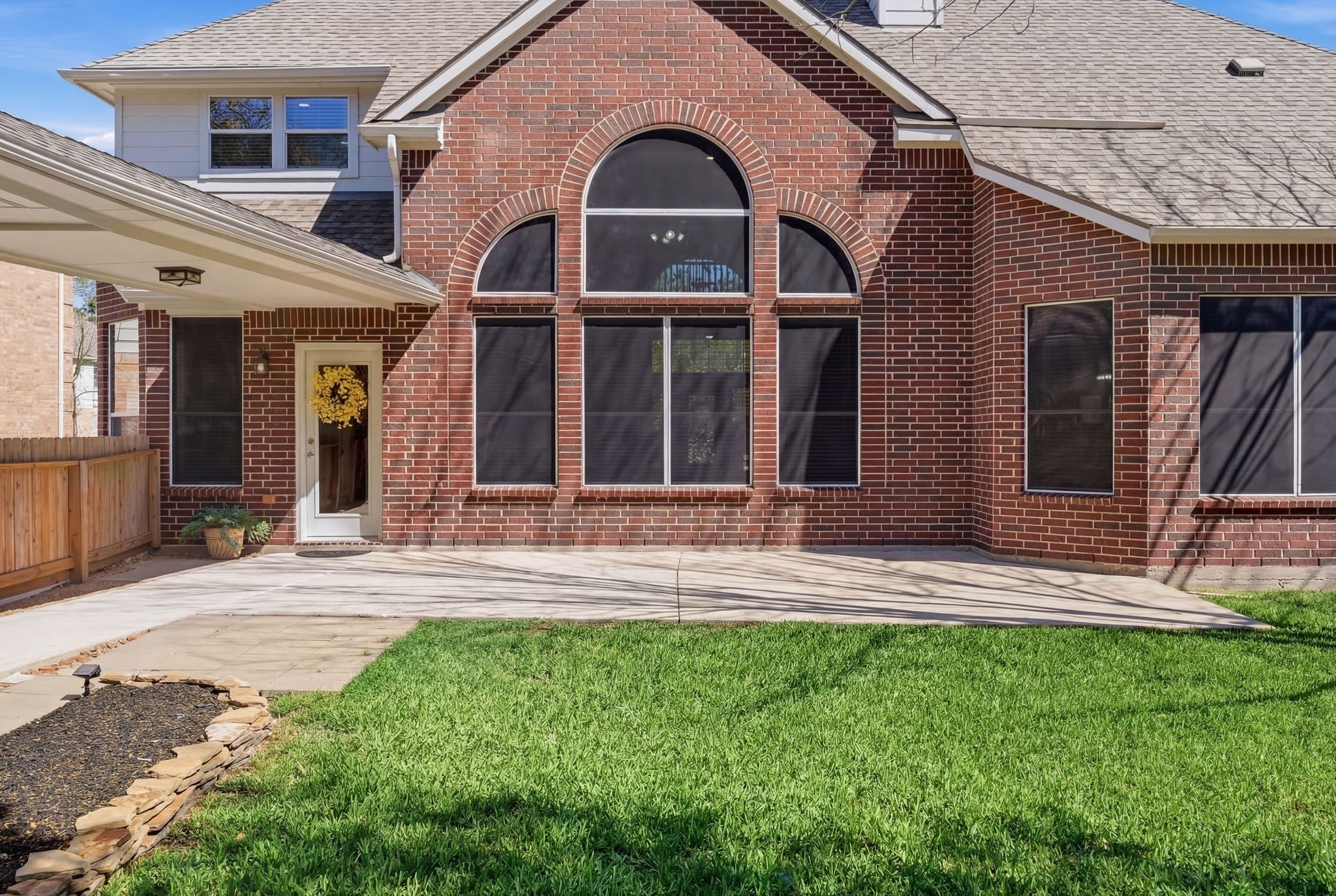 24931 Corbin Gate Drive Spring, TX 77389 - Photo 47 of 50 This home features a spacious brick exterior with large arched windows, and features a covered walk way leading to the detached 2 car garage. The backyard includes a well-maintained lawn, a concrete patio for outdoor gatherings, and is bordered by a wooden fence for privacy.