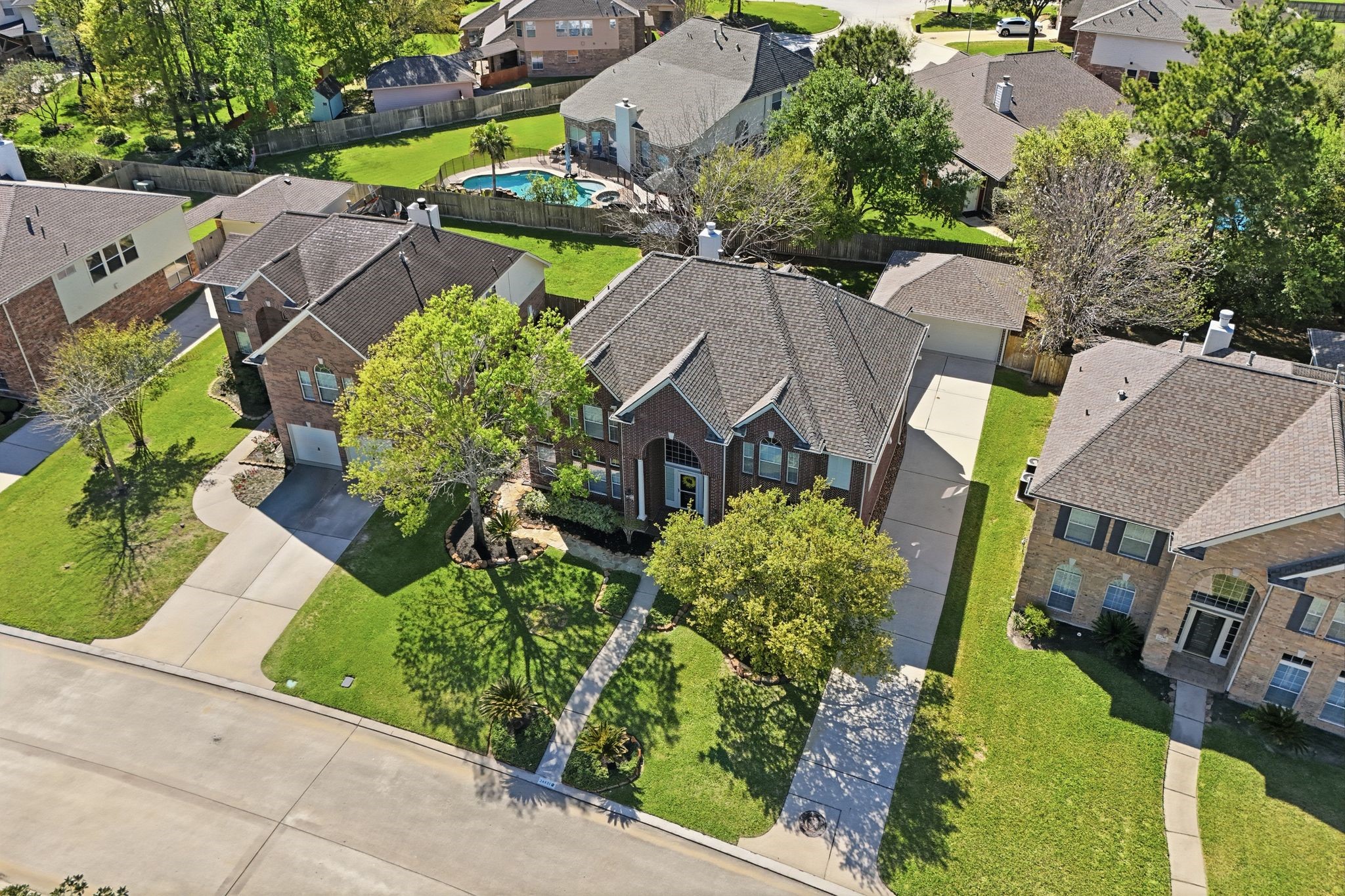24931 Corbin Gate Drive Spring, TX 77389 - Photo 49 of 50 This aerial view showcases a beautiful two-story brick home with a well-maintained front yard and mature trees. The property features a spacious driveway leading to a garage, and it's located in the Auburn Lakes neighborhood.