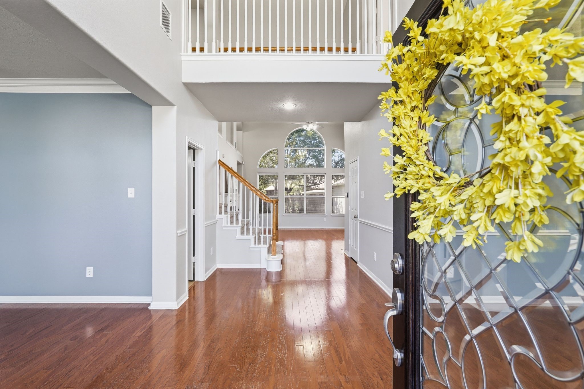 24931 Corbin Gate Drive Spring, TX 77389 - Photo 6 of 50 This inviting entryway features a stylish glass front door. The space boasts high ceilings, hardwood floors, and a view of a bright, open living area with large windows and a staircase leading to a second-floor landing.