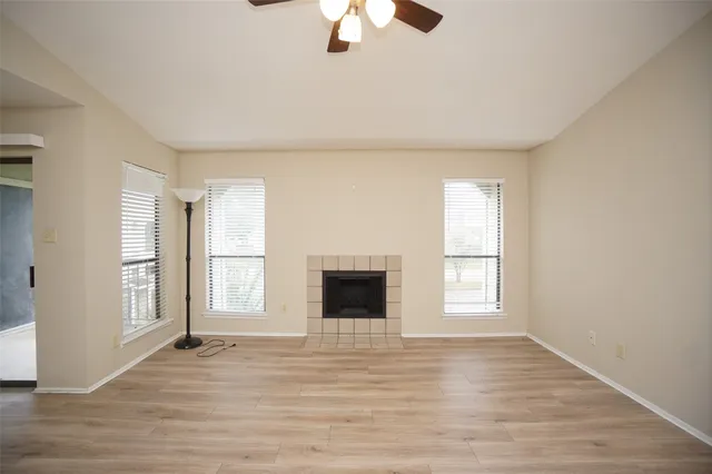 an empty room with wooden floor chandelier fan and windows
