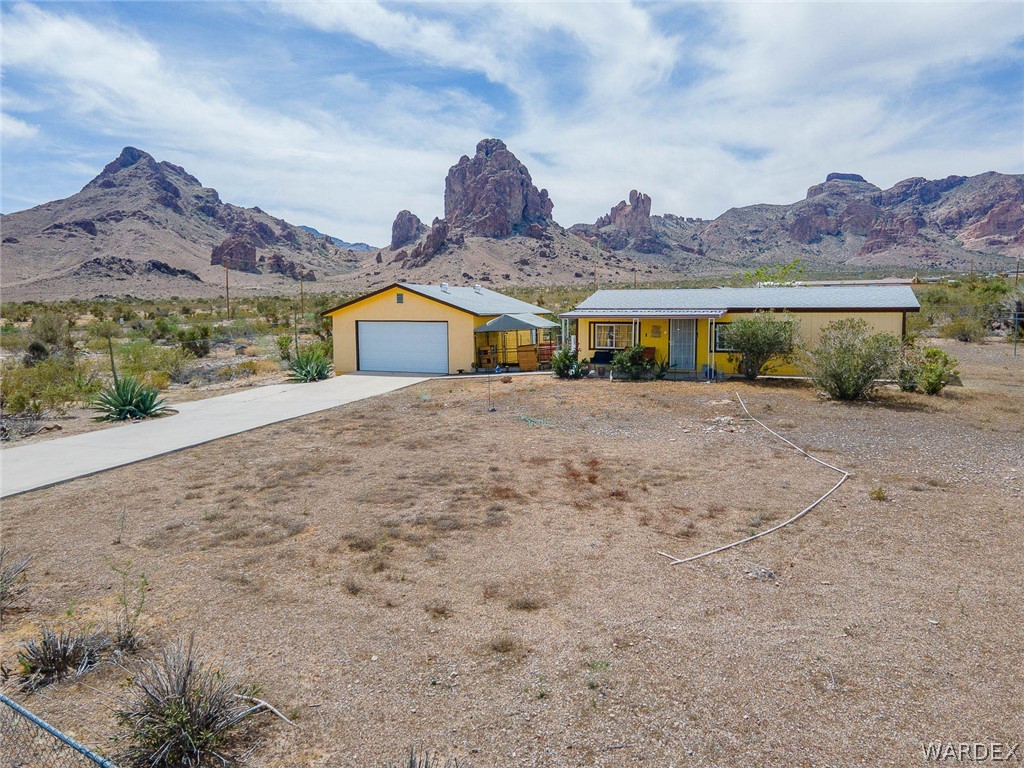 2465 Egar Road Golden Valley, AZ 86413 - Photo 70 of 98 The property features a single-story residence with a light-colored exterior and a detached garage, set against a mountainous backdrop
