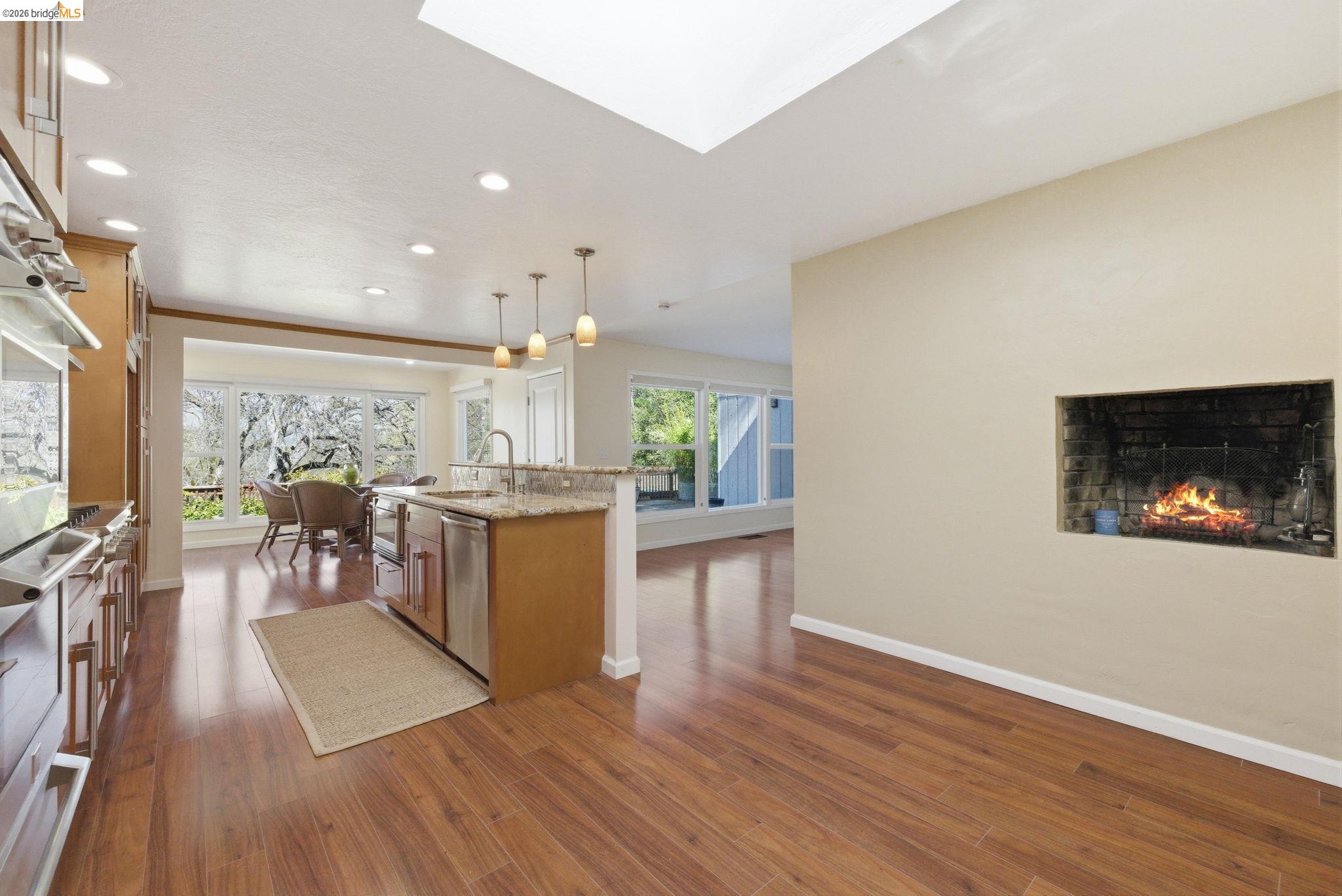 18389 Woodham Carne Road Sonora, CA 95370 - Photo 3 of 29 Kitchen featuring a kitchen island with sink, light stone countertops, dark wood-style flooring, pendant lighting, and a warm lit fireplace