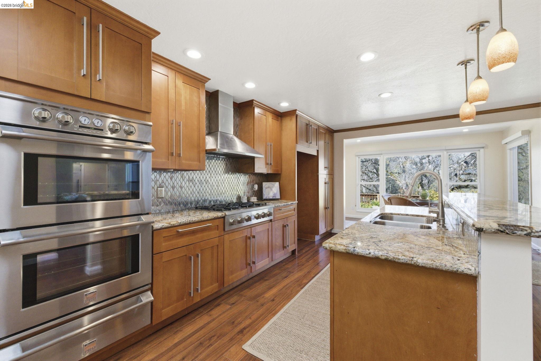 18389 Woodham Carne Road Sonora, CA 95370 - Photo 4 of 29 Kitchen with stainless steel appliances, wood finish cabinetry, a warming drawer, and light stone counters