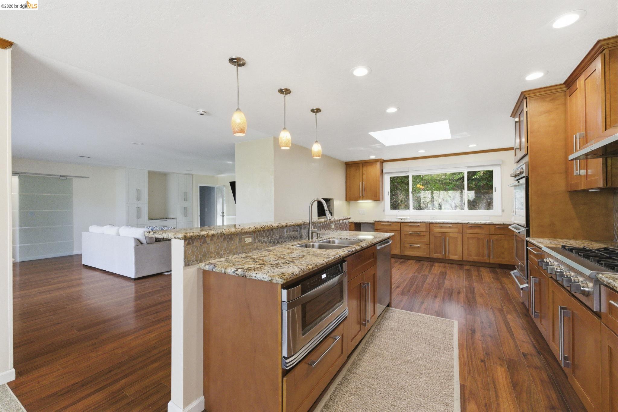 18389 Woodham Carne Road Sonora, CA 95370 - Photo 5 of 29 Kitchen with wood finish cabinetry, light stone counters, a skylight, an island with sink, and stainless steel appliances