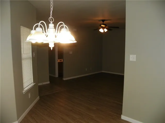 an empty room with wooden floor chandelier fan and windows