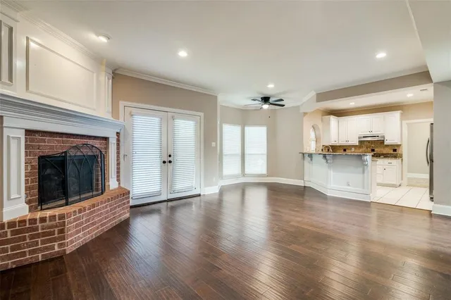 a view of an empty room and kitchen with wooden floor and a fireplace