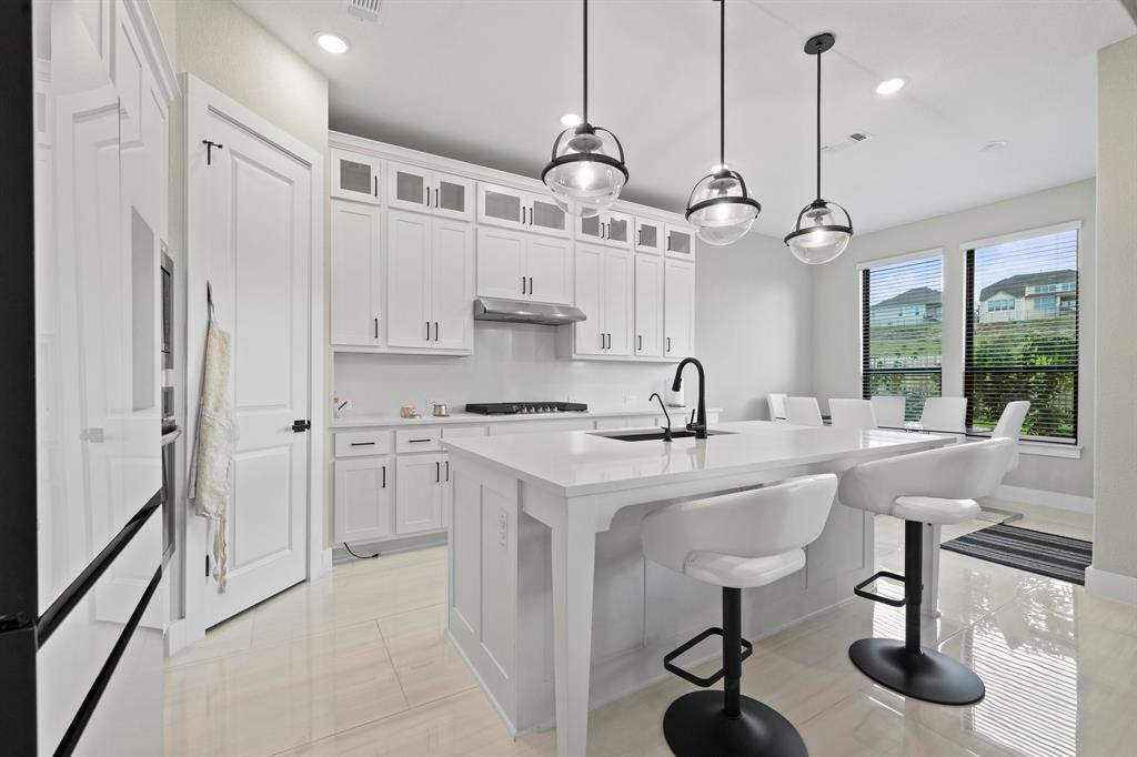 1008 Willie Rnch Way Leander, TX 78641 - Photo 17 of 40 Kitchen with white cabinetry, a kitchen bar, a kitchen island with sink, glass fronted cabinets, and hanging light fixtures