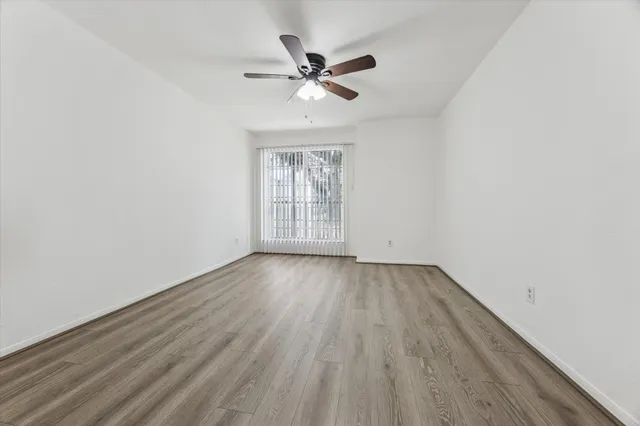 an empty room with wooden floor fan and windows