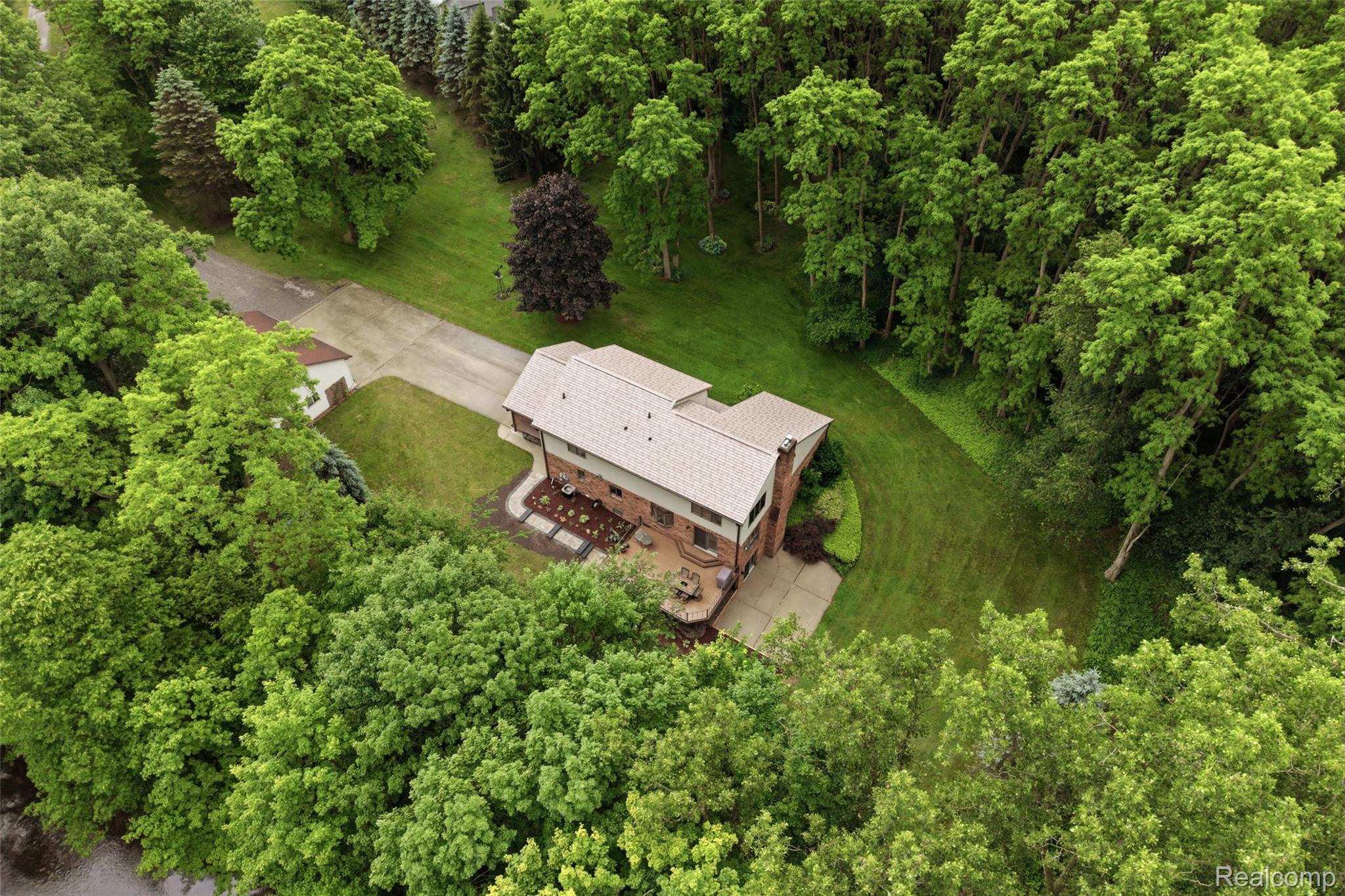 68345 Romeo Plank Road Ray, MI 48096 - Photo 14 of 52 Brick exterior residence with a light-colored roof, featuring a concrete patio, established landscaping, and a driveway leading to a detached structure