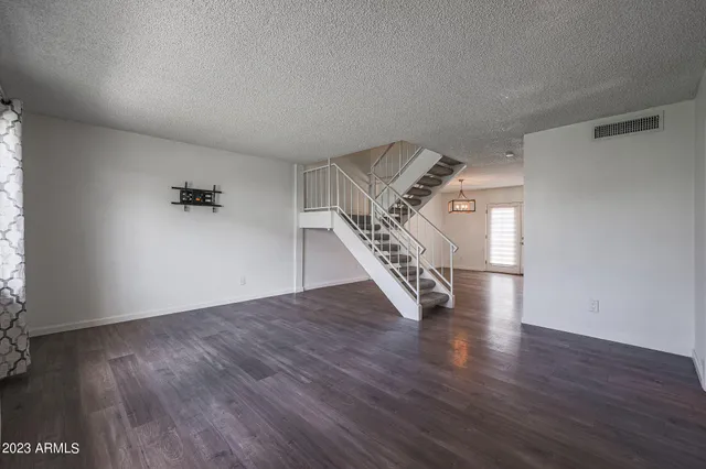 an empty room with wooden floor staircase and windows