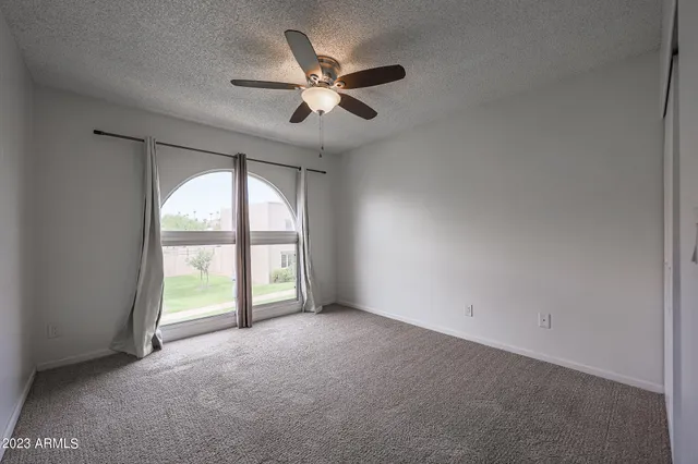 an empty room with chandelier fan and windows