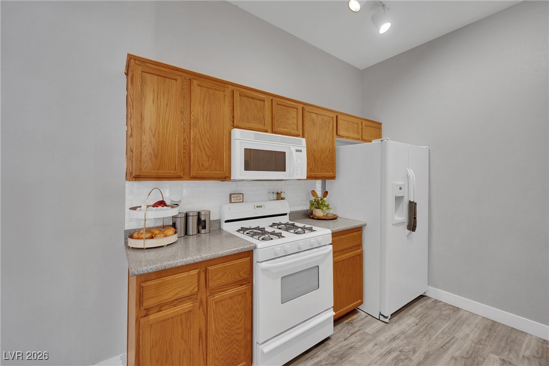 3544 Desert Cliff Street, Unit 101 Las Vegas, NV 89129 - Photo 15 of 29 Kitchen featuring white appliances, light countertops, decorative backsplash, and light wood-type flooring