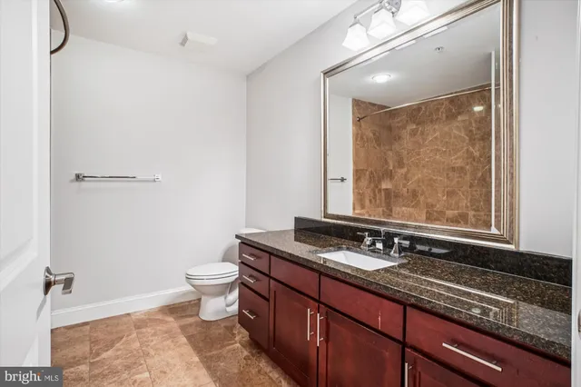 a bathroom with a granite countertop sink a toilet a mirror and shower