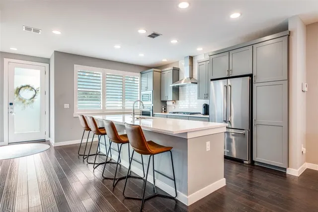 a kitchen with stainless steel appliances granite countertop a dining table chairs refrigerator and wooden floor