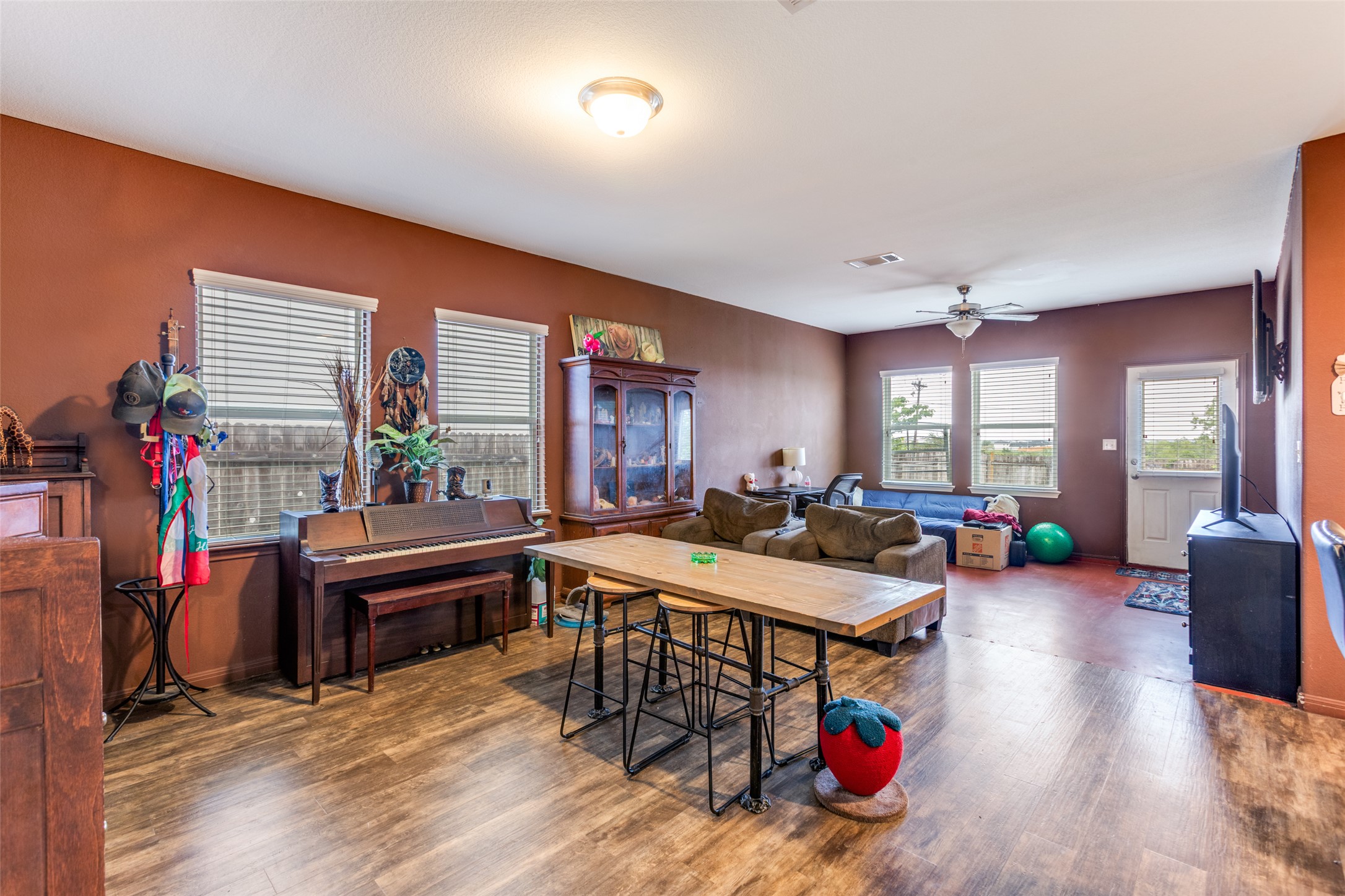 13909 Sherri Berry Way Manor, TX 78653 - Photo 13 of 28 Spacious open-concept room featuring wood-finish flooring, multiple windows with blinds, a ceiling fan, and direct exterior access