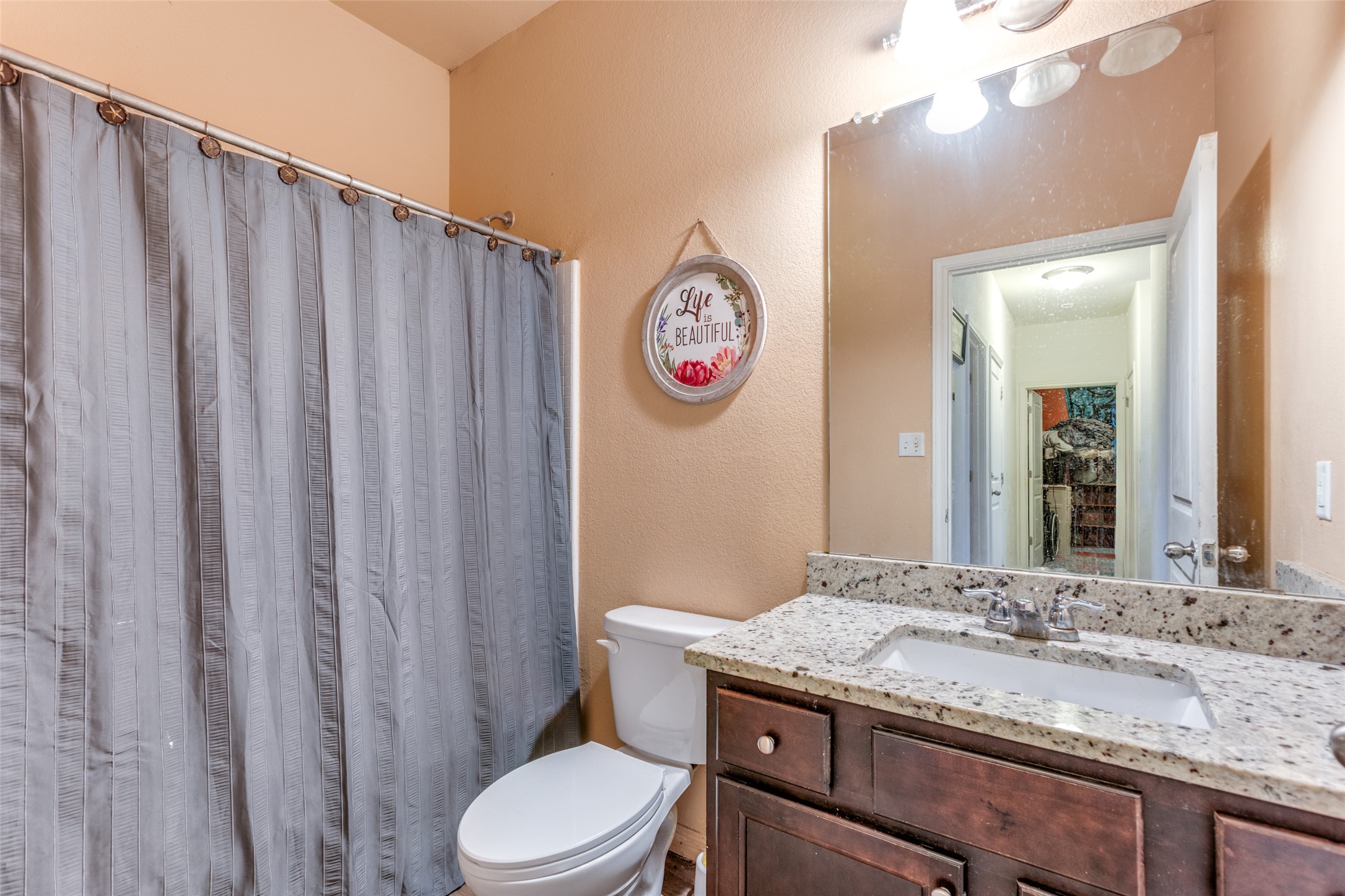 13909 Sherri Berry Way Manor, TX 78653 - Photo 18 of 28 Bathroom featuring a dark wood-finish vanity with a light speckled countertop, an undermount sink, and a wall-mounted mirror with overhead lighting