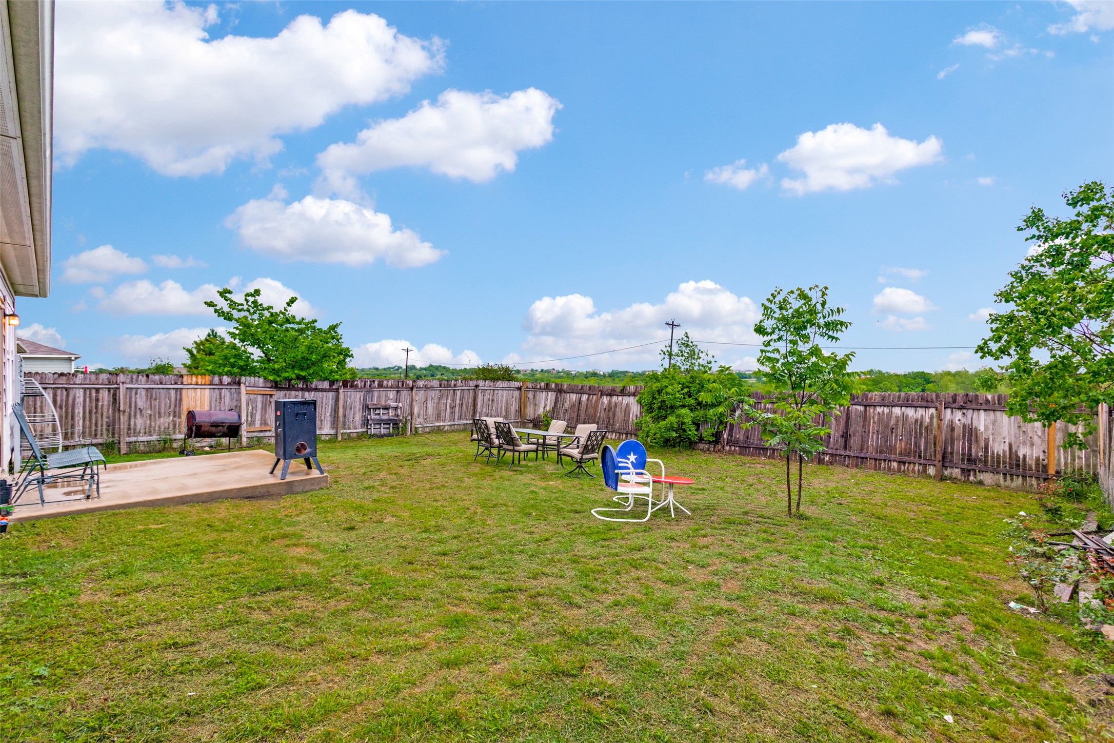 13909 Sherri Berry Way Manor, TX 78653 - Photo 20 of 28 Expansive grassy backyard featuring a concrete patio, wood privacy fencing, and mature trees