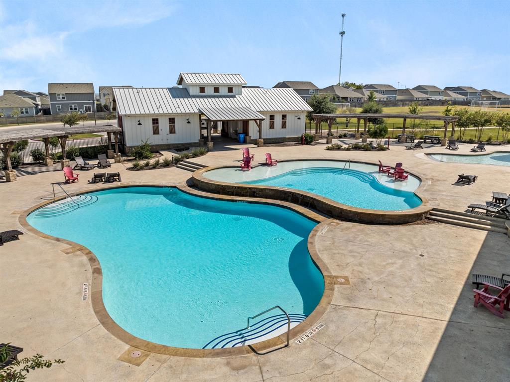 13909 Sherri Berry Way Manor, TX 78653 - Photo 25 of 28 Pool area featuring multiple swimming pools with integrated steps, surrounding concrete decking, and a white-sided building with a metal roof