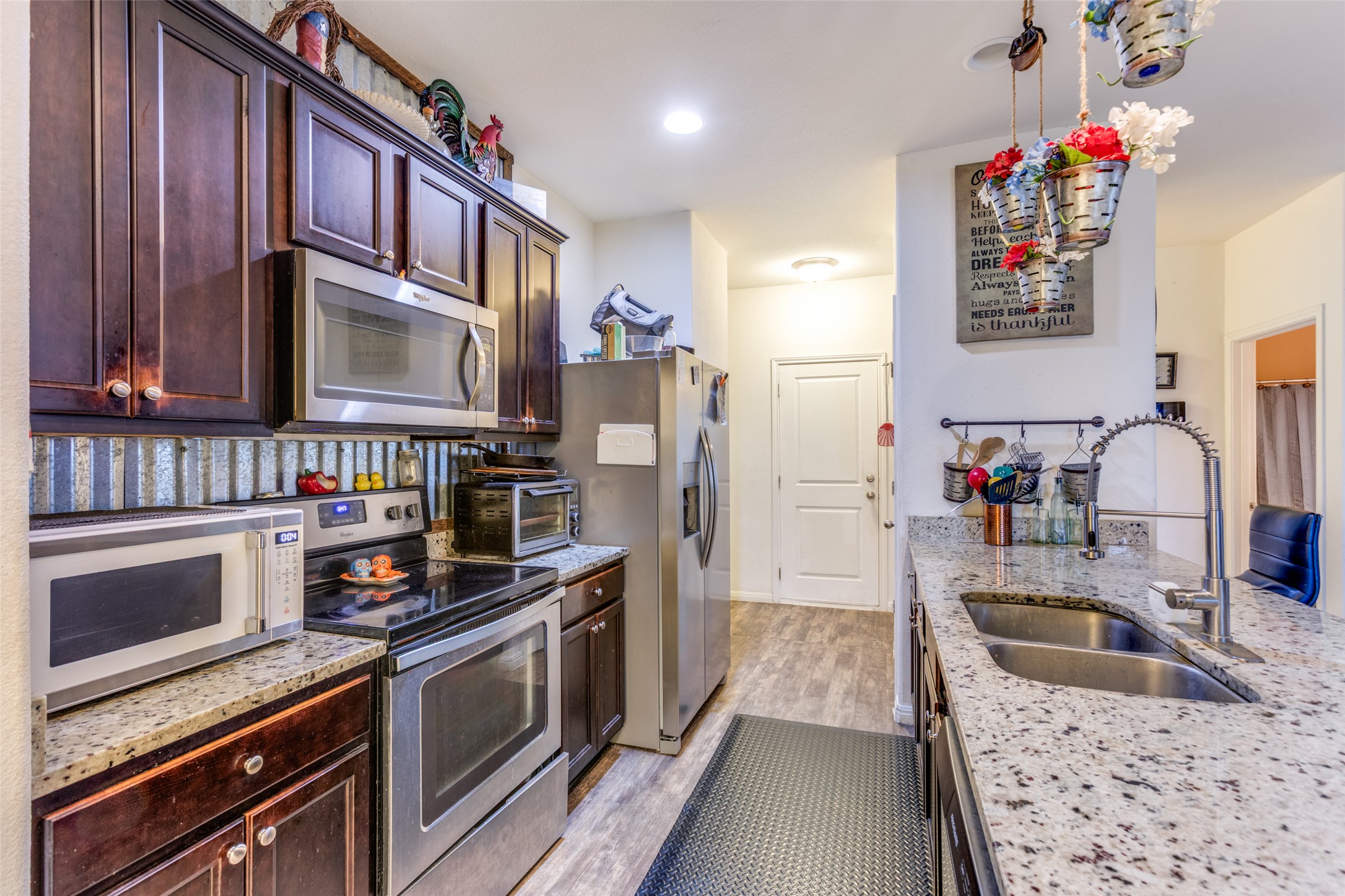13909 Sherri Berry Way Manor, TX 78653 - Photo 4 of 28 Kitchen featuring granite countertops, wood-finish flooring, stainless steel appliances, dark wood cabinetry, and a double basin sink with a gooseneck faucet