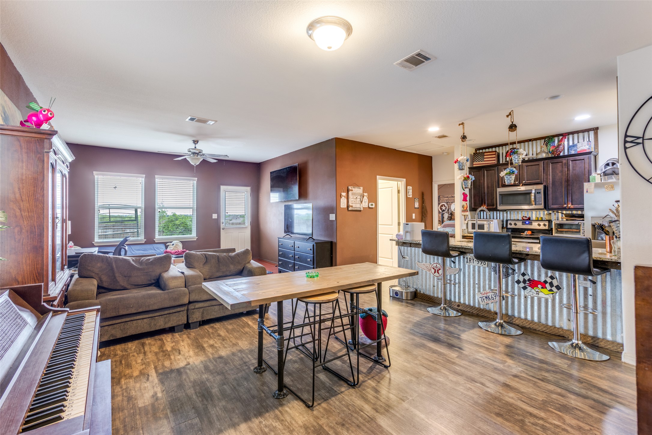 13909 Sherri Berry Way Manor, TX 78653 - Photo 7 of 28 Open-concept living space featuring wood-finish flooring, a kitchen island with seating, dark wood cabinetry, stainless steel appliances, and multiple windows