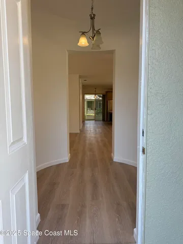 a view of a hallway to an empty room with wooden floor and a window