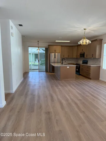 a view of a kitchen with kitchen island a counter top space a sink wooden floor and window
