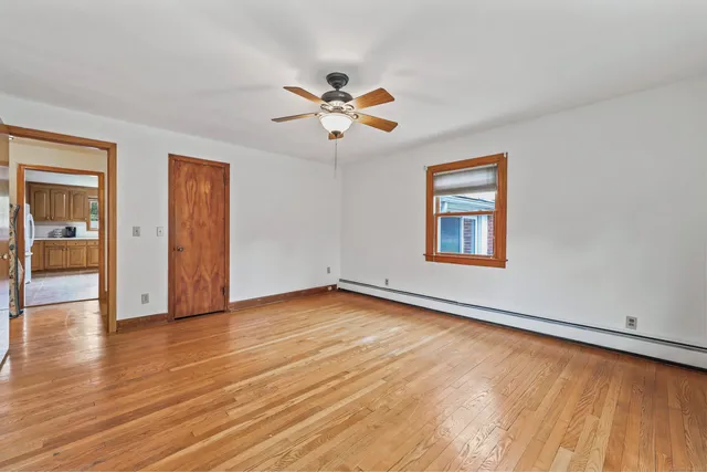 an empty room with wooden floor chandelier fan and windows