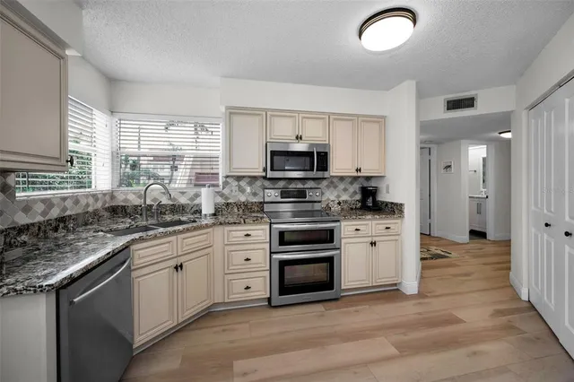 a kitchen with stainless steel appliances granite countertop a stove top oven a sink dishwasher a refrigerator and a microwave oven with wooden floor