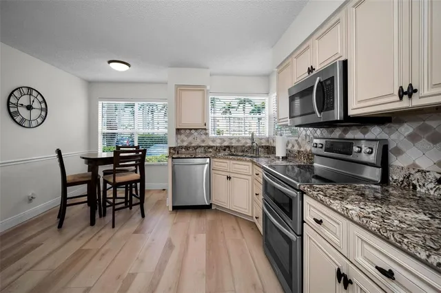 a kitchen with stainless steel appliances granite countertop a stove top oven a sink dishwasher and white cabinets with wooden floor