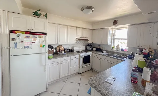 a kitchen with a refrigerator a sink dishwasher and white cabinets next to a window