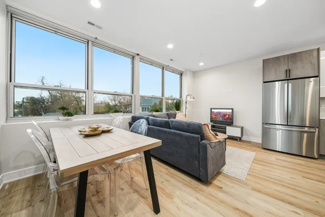 a living room with stainless steel appliances furniture a large window and a wooden floor
