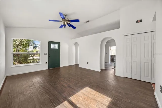 an empty room with wooden floor fan and windows