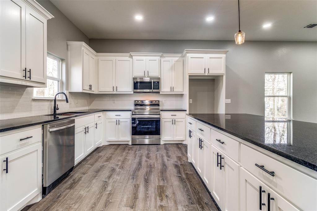 a large kitchen with stainless steel appliances granite countertop a stove a sink and white cabinets