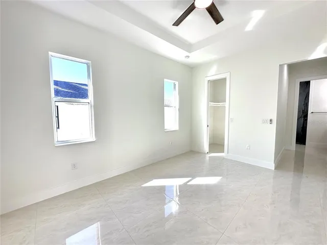 an empty room with chandelier fan and windows