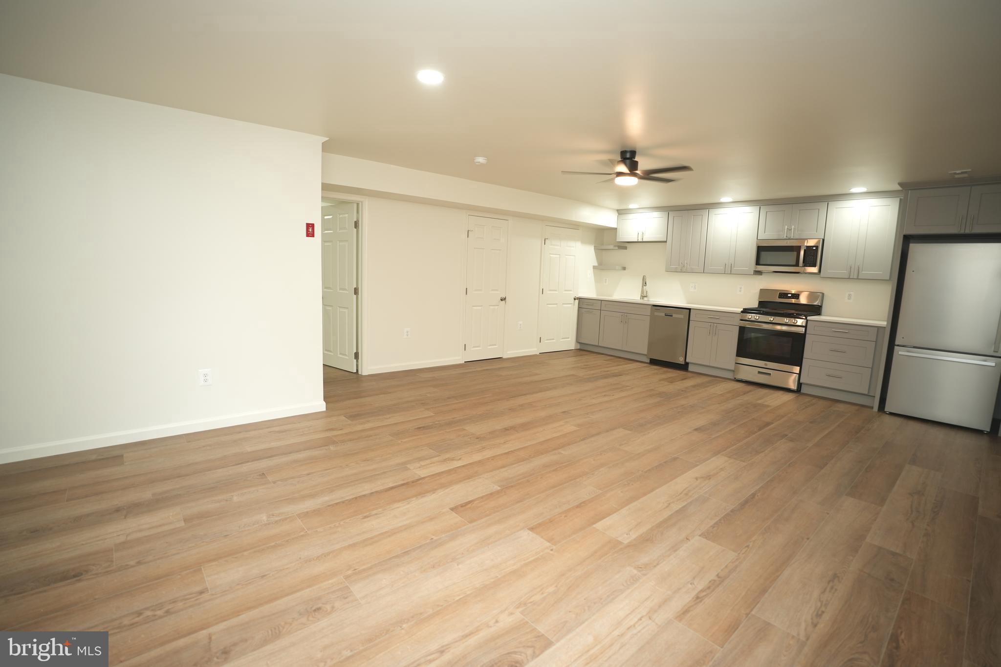 22271 Goldenrod Drive, Unit BASEMENT APARTMENT Great Mills, MD 20634 - Photo 4 of 15 an empty room with wooden floor ceiling fan and kitchen view