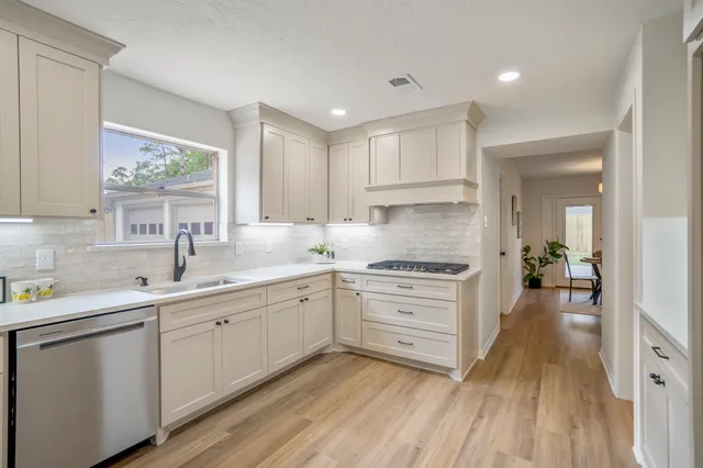 a kitchen with white cabinets a sink dishwasher and a stove with wooden floor