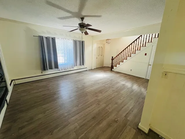 an empty room with wooden floor stairs and a chandelier fan