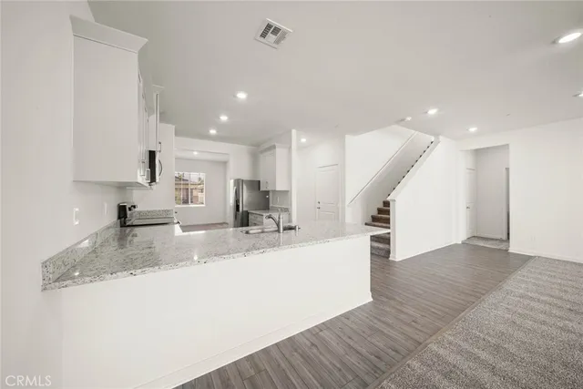 a large kitchen with stainless steel appliances granite countertop a sink dishwasher a refrigerator and white cabinets with wooden floor