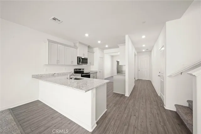 a kitchen with a sink a refrigerator a stove and white cabinets with wooden floor