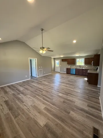 an empty room with wooden floor kitchen view and a window