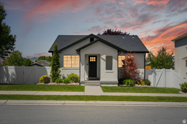 11892 Preamble Road Draper, UT 84020 - Photo 1 of 1 Stucco exterior with black trim accents, a black-paneled entry door, mature landscaping, a concrete pathway, and a white vinyl fence enclosing the property