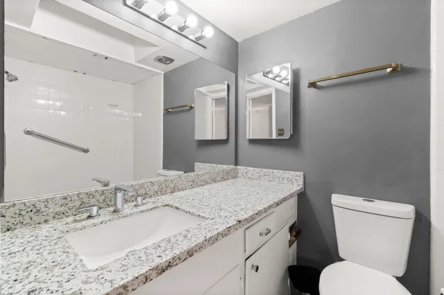 a bathroom with a granite countertop sink a toilet and a mirror