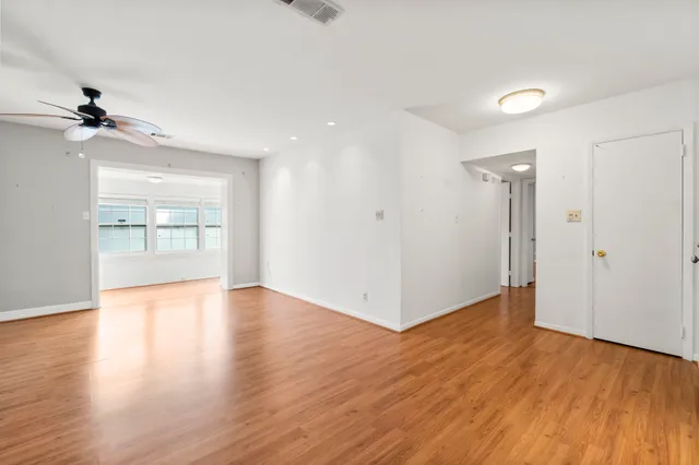 an empty room with wooden floor ceiling fan and windows