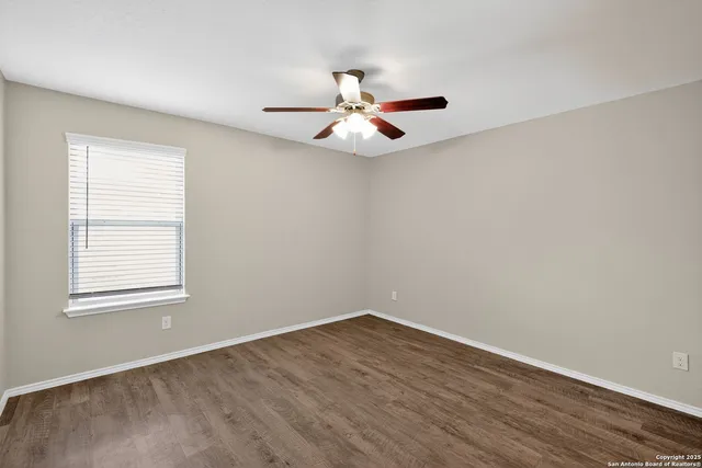 an empty room with wooden floor ceiling fan and window