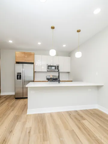 a large kitchen with kitchen island a stove a sink a refrigerator white cabinets and wooden floor