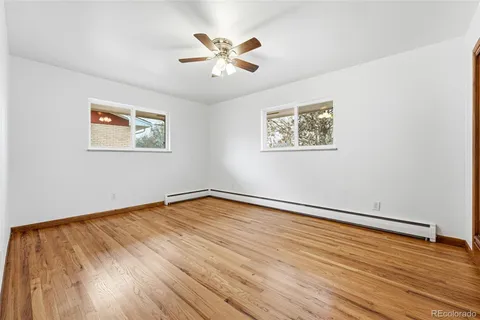 a view of an empty room with wooden floor and a ceiling fan