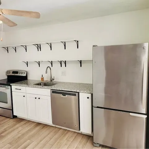 a kitchen with granite countertop a refrigerator a sink and white cabinets
