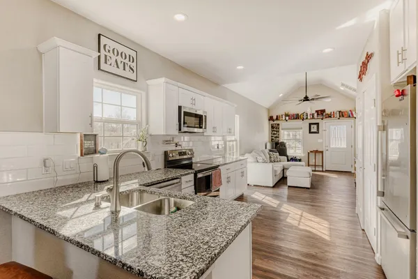 a kitchen with stainless steel appliances granite countertop a sink dishwasher stove and white cabinets with wooden floor