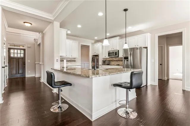 a kitchen with stainless steel appliances kitchen island granite countertop a refrigerator a stove and white cabinets with wooden floor