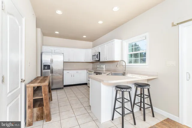 a kitchen with stainless steel appliances granite countertop a stove a sink a refrigerator and white cabinets with wooden floor